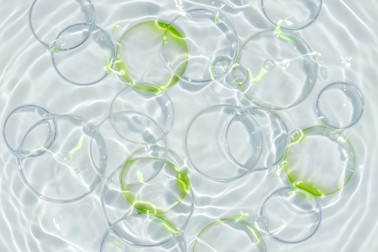 Transparent circles in bright shimmering water with green reflections.