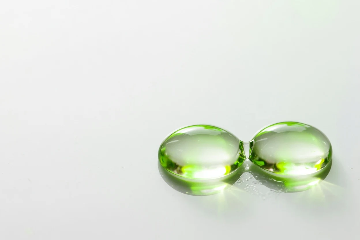 Two joined clear droplets on a white background with green reflections.